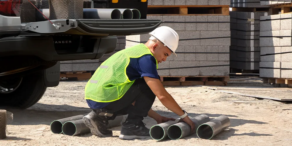 low angle close up of a worker beside dark pipes with bright neon green and neutral construction
